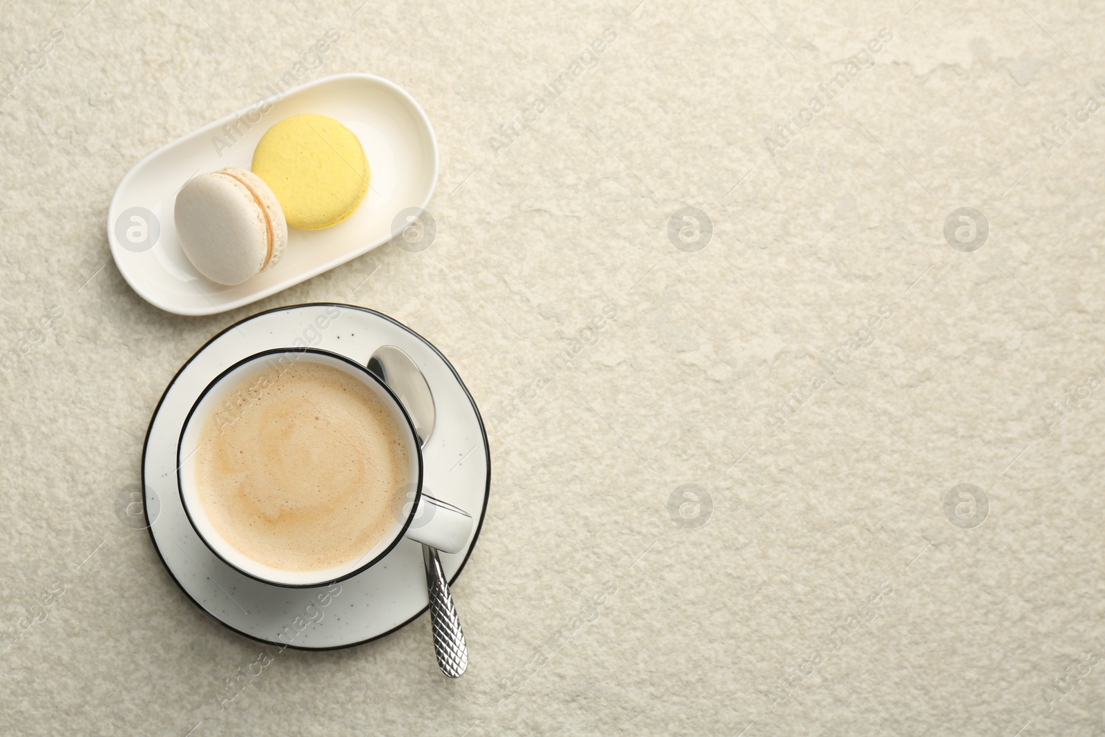 Photo of Tasty cappuccino in cup and macarons on light textured table, flat lay. Space for text