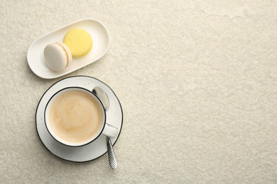 Photo of Tasty cappuccino in cup and macarons on light textured table, flat lay. Space for text