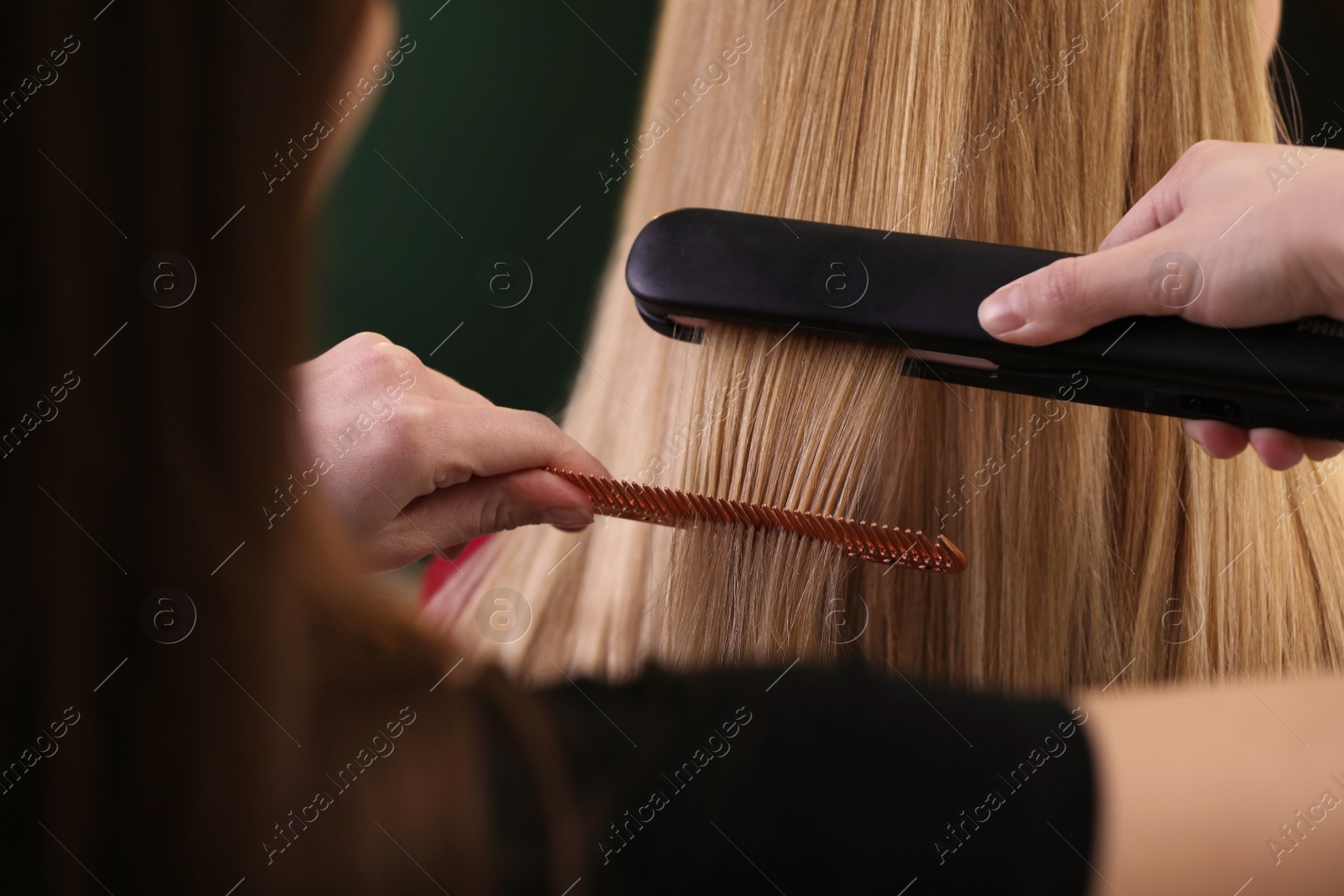 Photo of Stylist straightening woman's hair with flat iron in salon, closeup