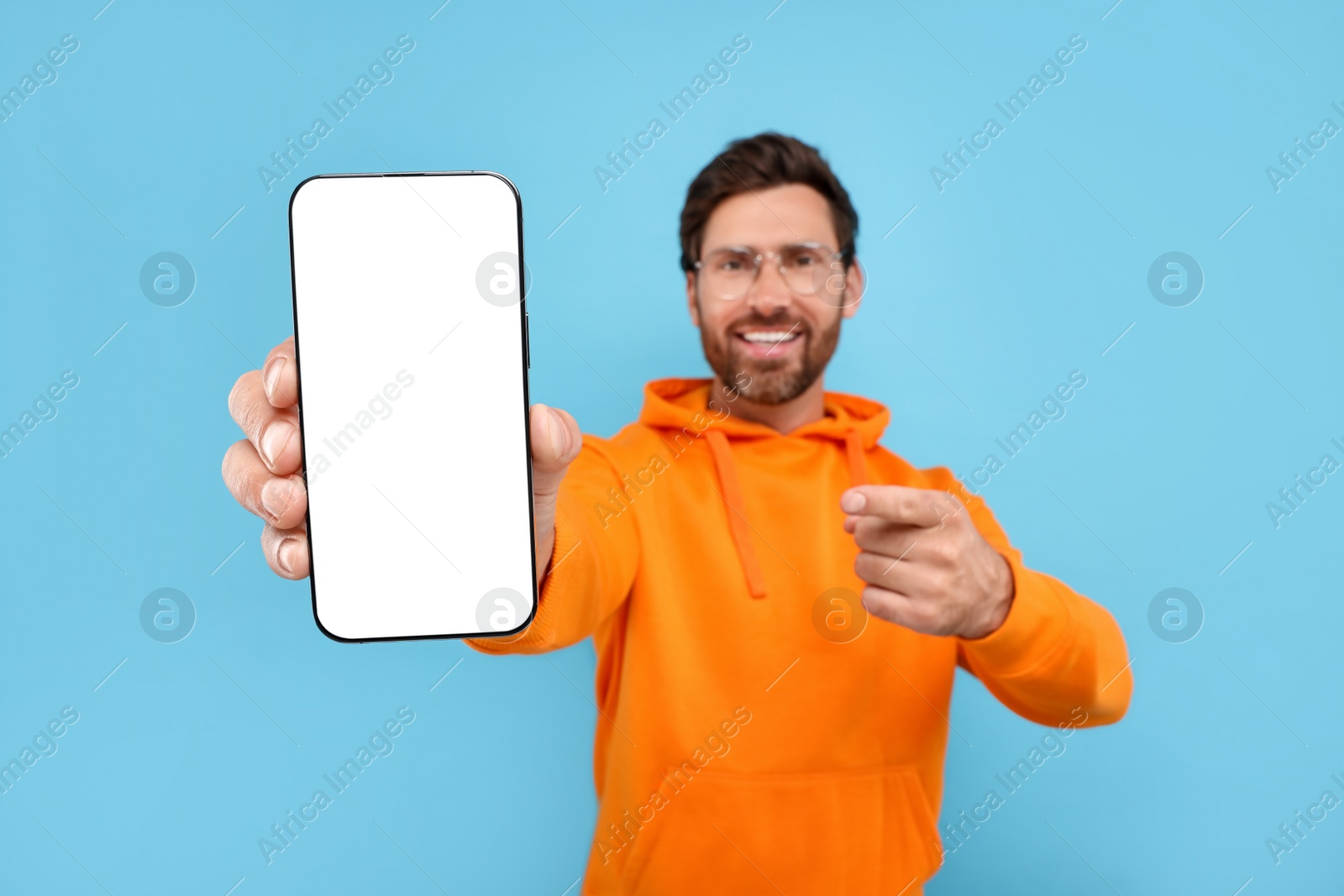 Photo of Handsome man showing smartphone in hand and pointing at it on light blue background, selective focus. Mockup for design
