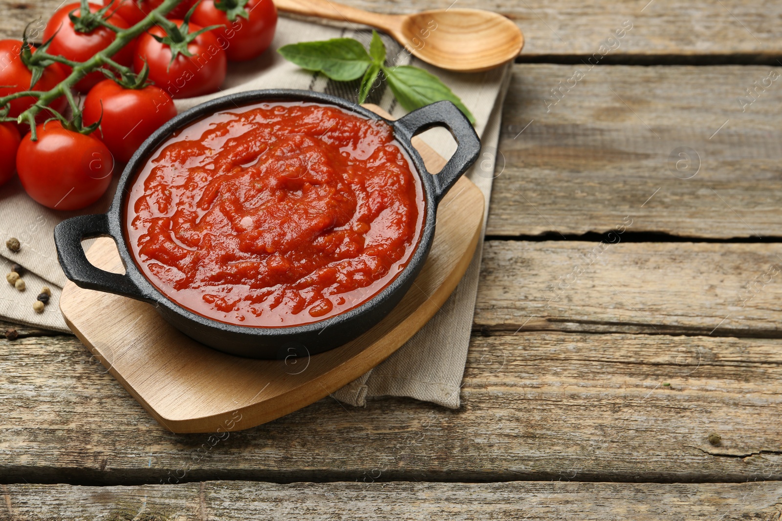 Photo of Homemade tomato sauce in bowl, spoon and ingredients on wooden table, space for text