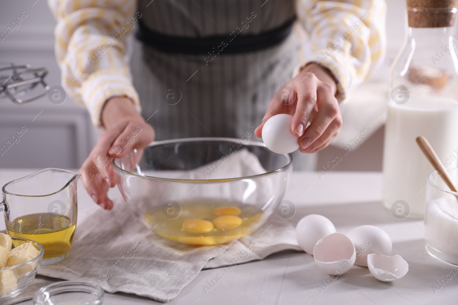 Photo of Making dough. Woman breaking egg at white table in kitchen, closeup