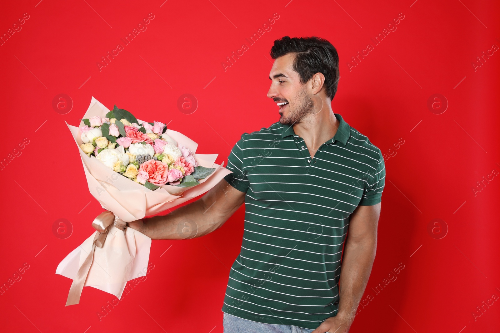 Photo of Young handsome man with beautiful flower bouquet on red background