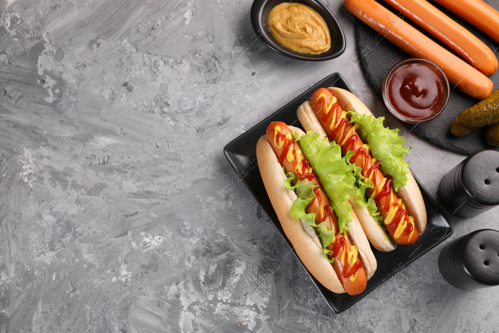 Photo of Tasty hot dogs and ingredients on grey textured table, flat lay. Space for text