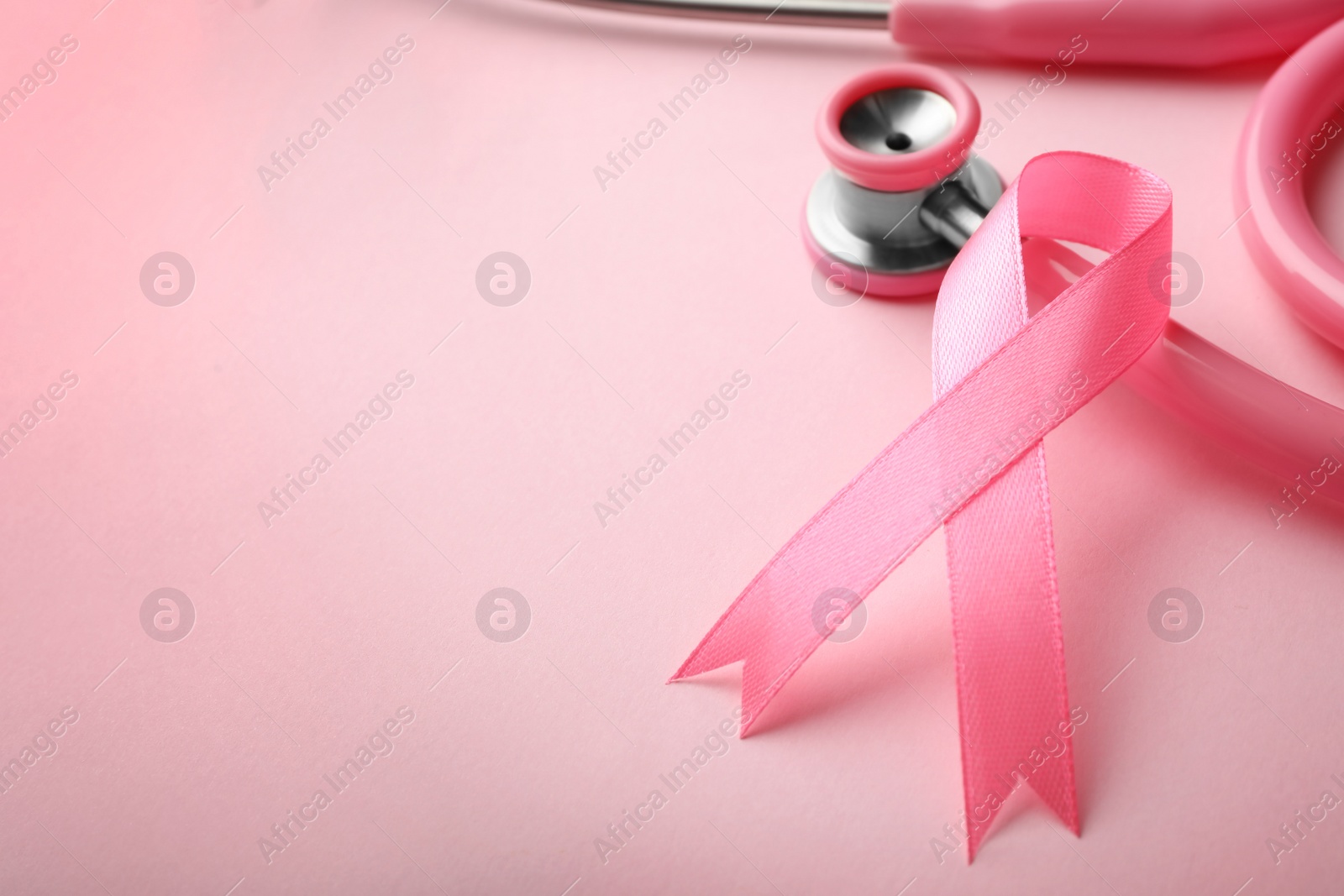 Photo of Pink ribbon and stethoscope on color background, space for text. Breast cancer concept