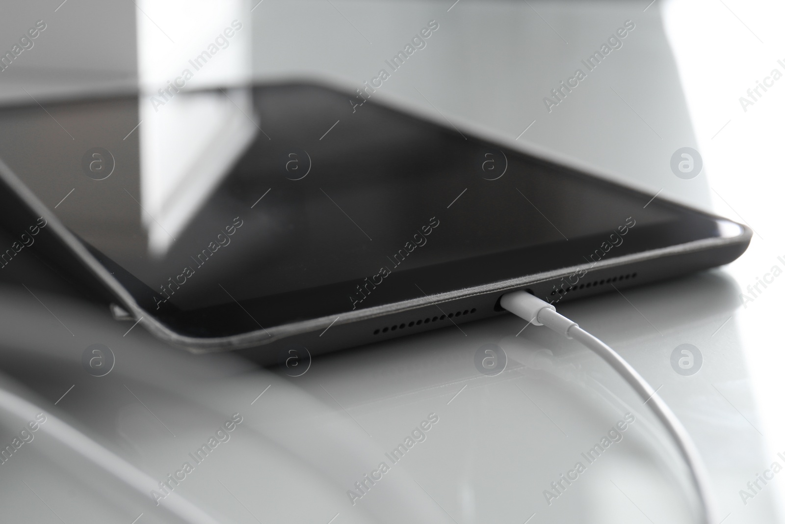 Photo of Tablet charging on white table, closeup view