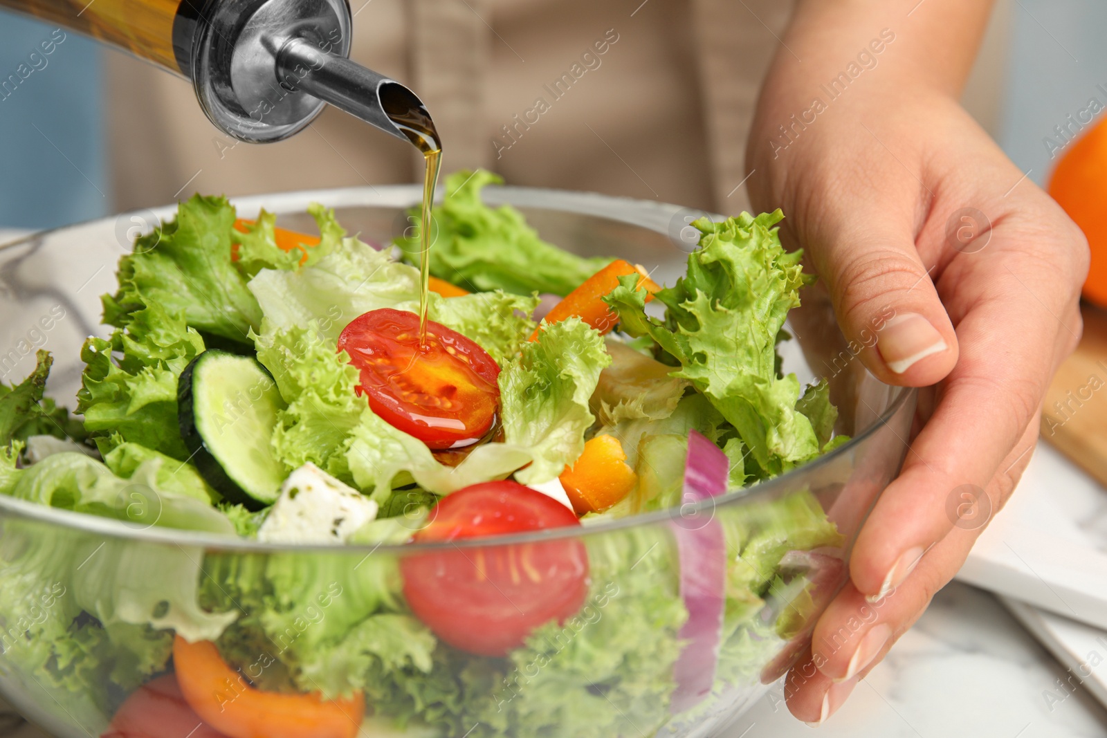 Photo of Woman dressing tasty fresh Greek salad with olive oil at table, closeup