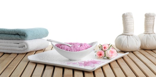 Photo of Bowl of pink sea salt, beautiful roses, herbal bags and towels on wooden table against white background