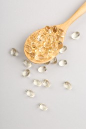 Photo of Wooden spoon with vitamin capsules on light background, top view