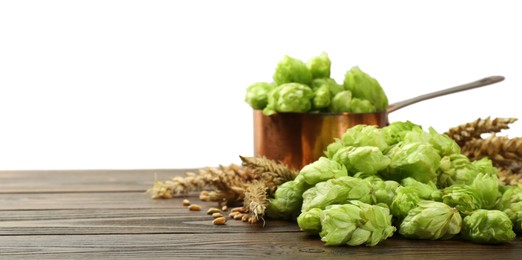 Photo of Fresh hop flowers and wheat ears on wooden table against white background, space for text