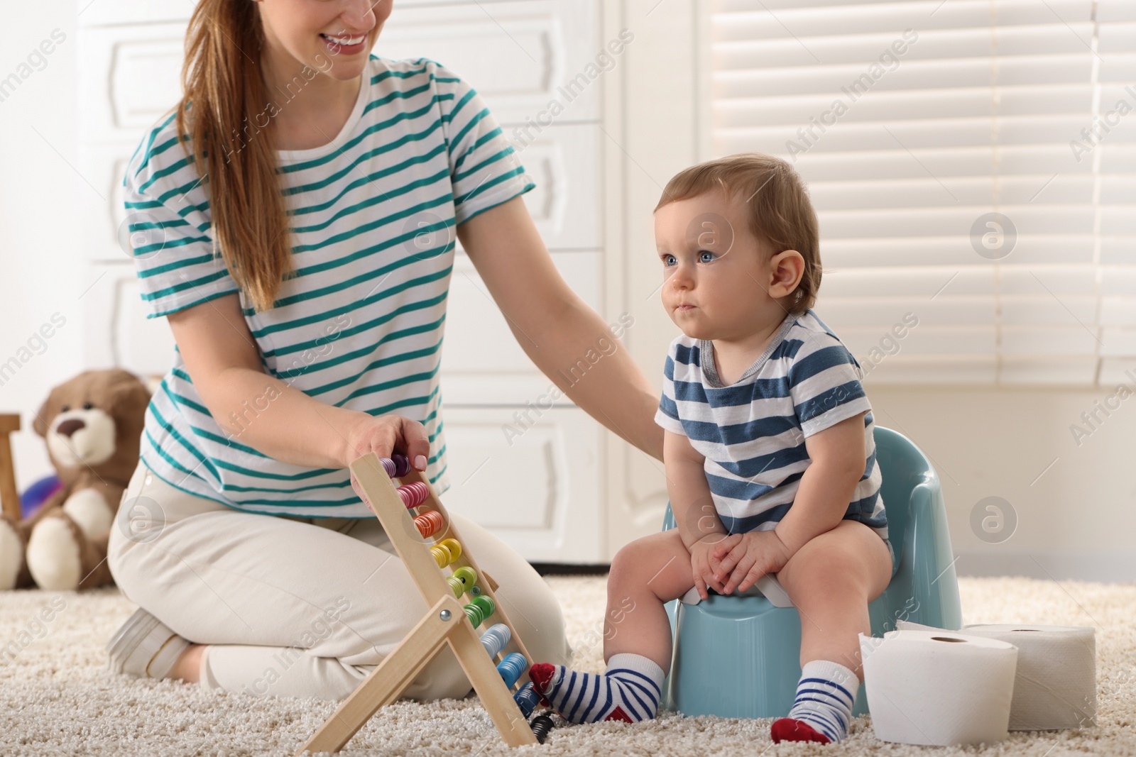 Photo of Mother training her child to sit on baby potty indoors