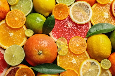 Photo of Sliced and whole citrus fruits with leaves as background, top view