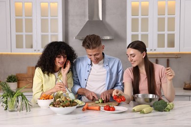 Friends cooking healthy vegetarian meal at white marble table in kitchen