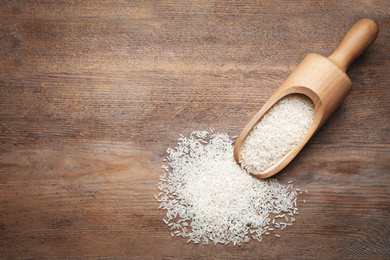 Photo of Uncooked rice and scoop on wooden table, top view. Space for text