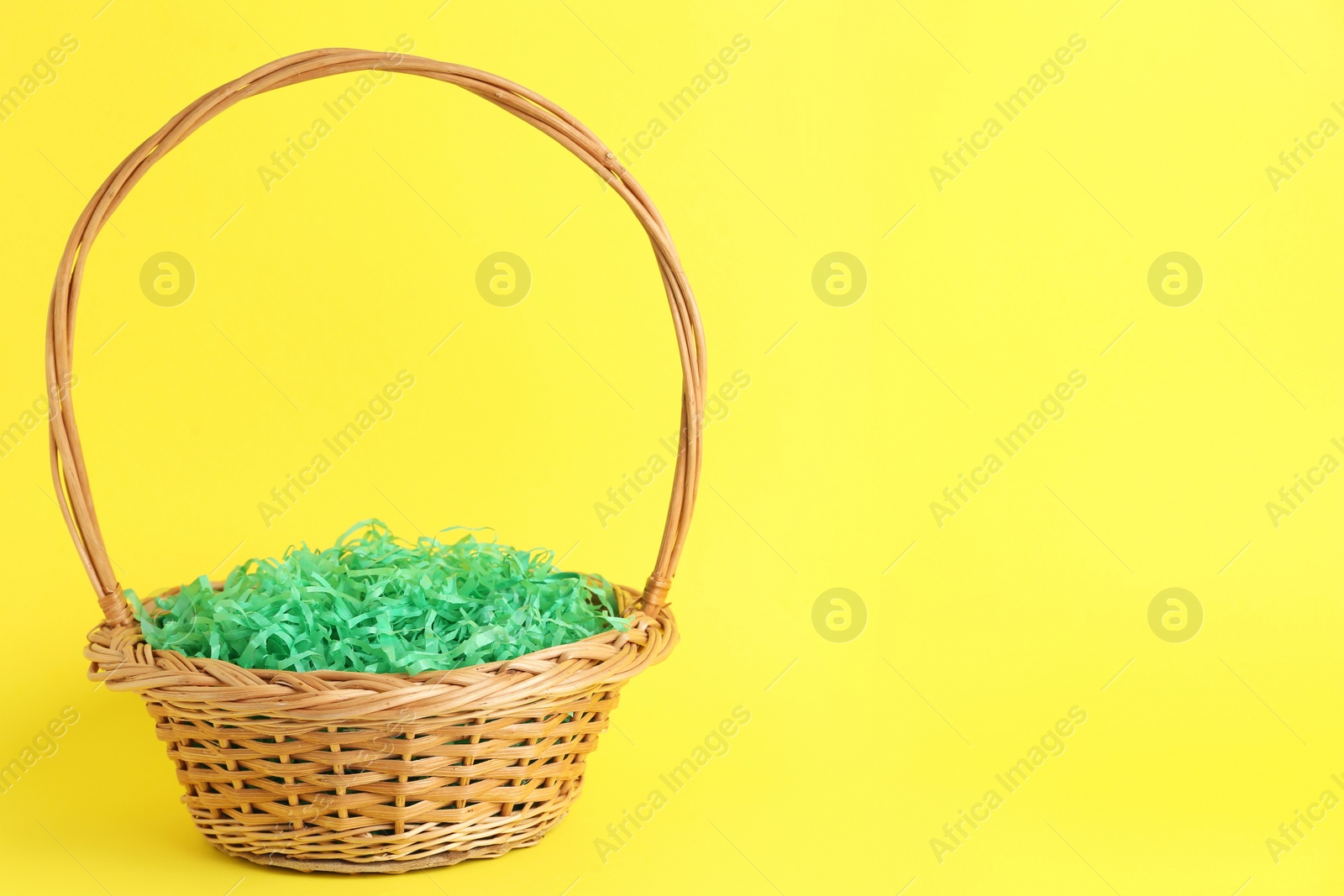 Photo of Easter basket with green paper filler on yellow background, space for text