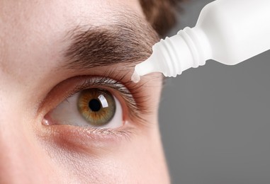 Image of Man applying eye drops on grey background, closeup