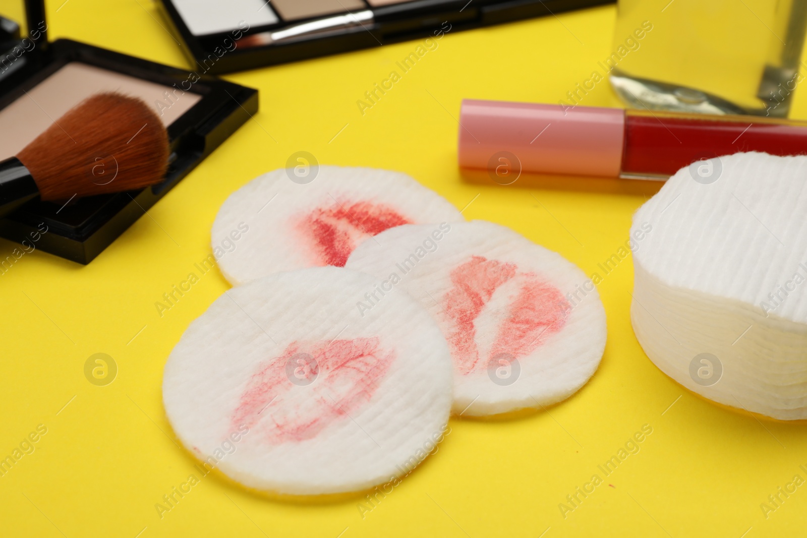 Photo of Dirty cotton pads after removing makeup and different products on yellow background, closeup