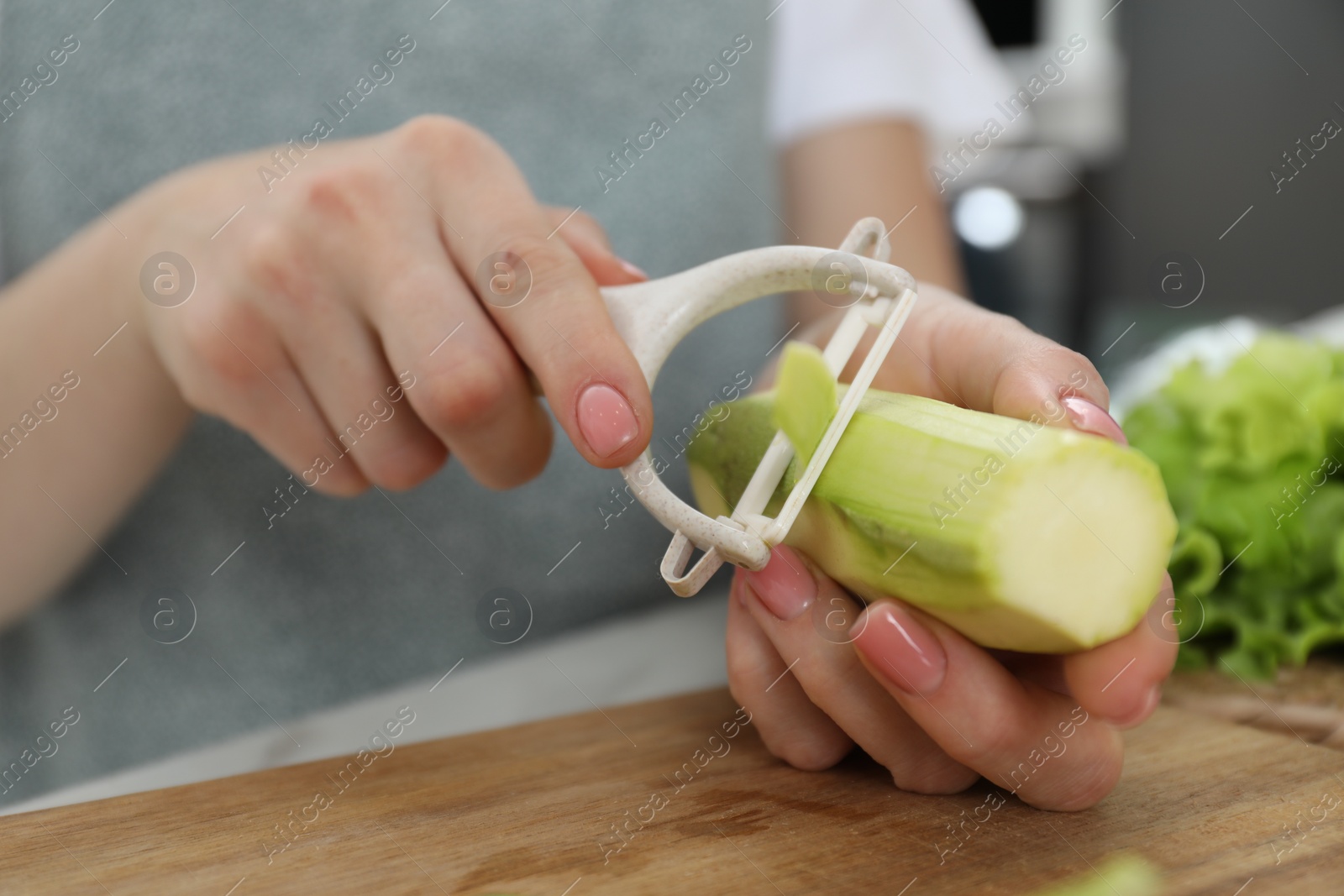 Photo of Woman peeling fresh zucchini at table, closeup