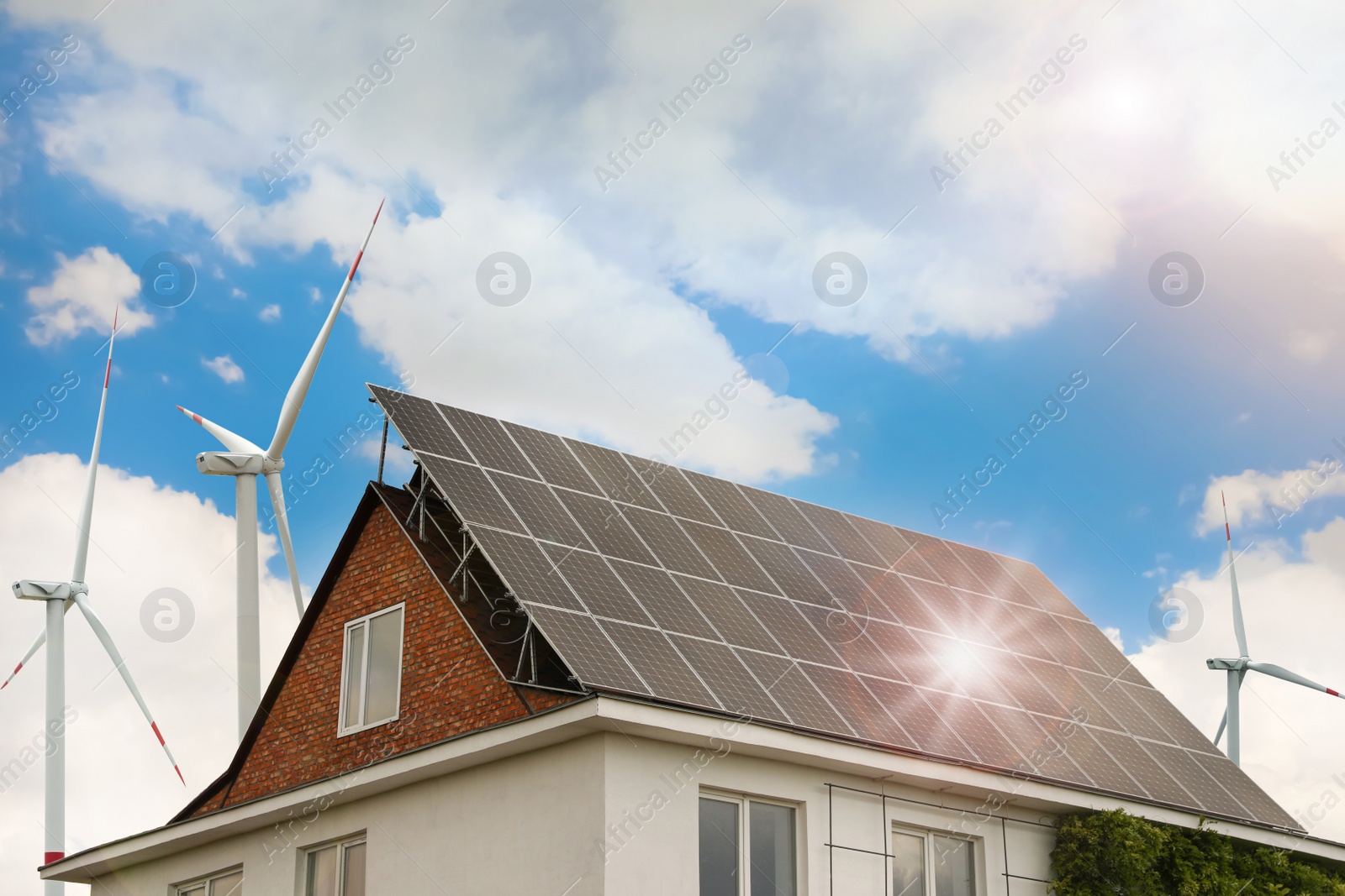 Image of Wind turbines near house with installed solar panels on roof. Alternative energy source