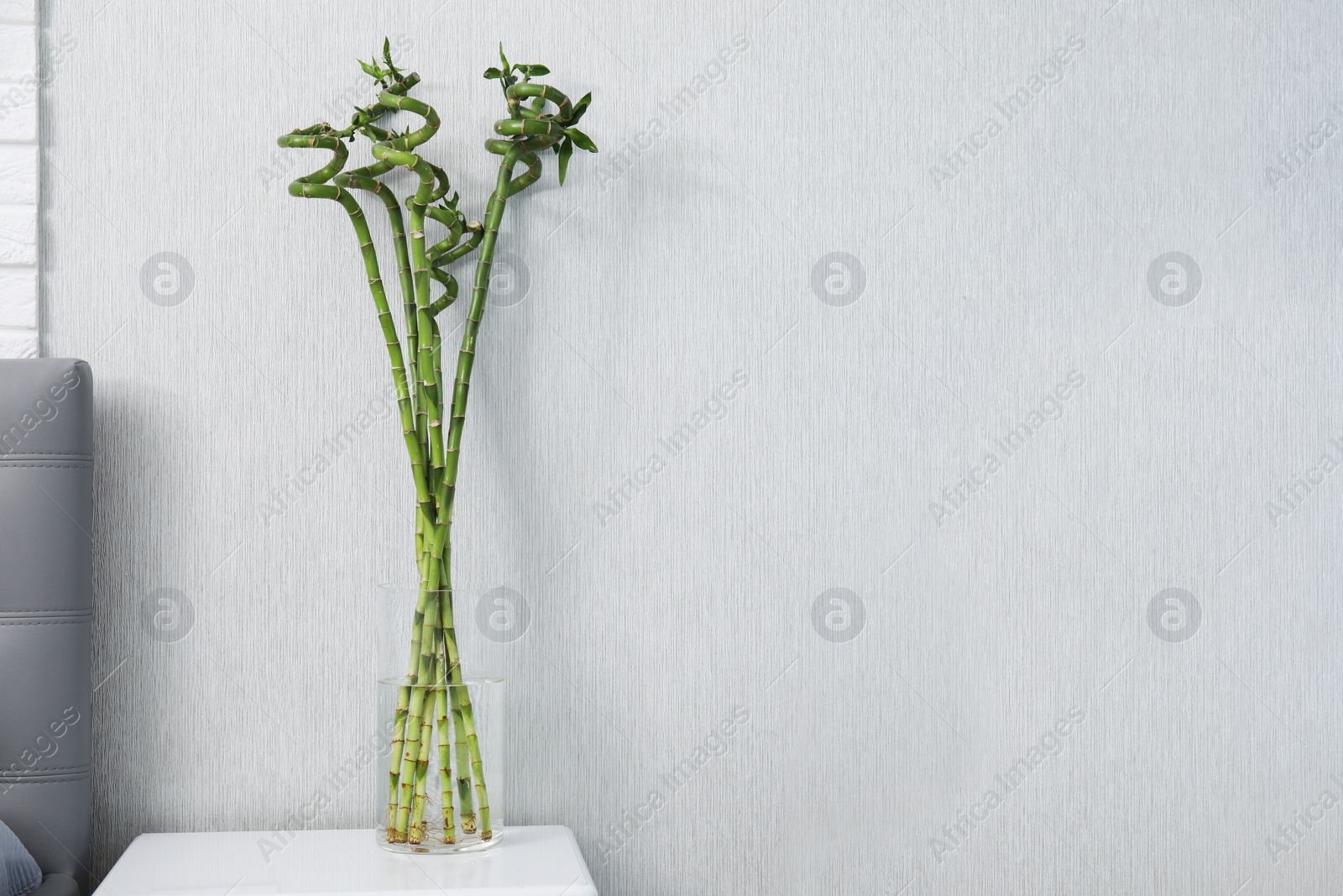 Photo of Vase with beautiful green bamboo stems on white bedside table indoors