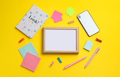 Photo of Blank white board with stationery and smartphone on yellow background, flat lay. Space for text