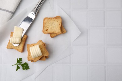 Photo of Tasty butter curls, knife and pieces of dry bread on white tiled table, flat lay. Space for text
