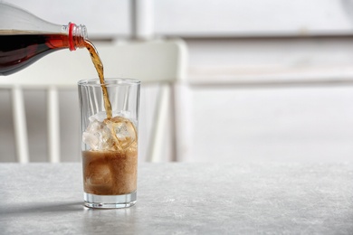Photo of Pouring cola from bottle into glass on table. Space for text