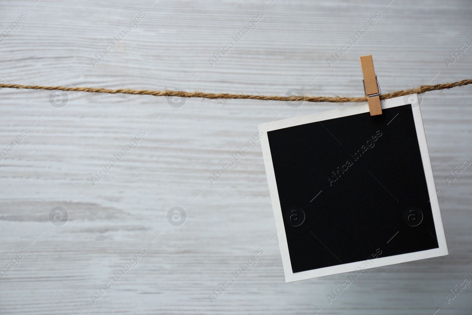 Photo of Clothespin with empty instant frame on twine against white wooden background. Space for text