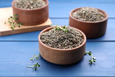 Photo of Bowls with dried and fresh thyme on blue wooden table, closeup