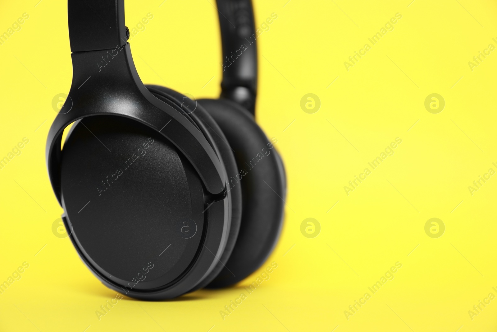 Photo of Modern wireless headphones on yellow background, closeup. Space for text