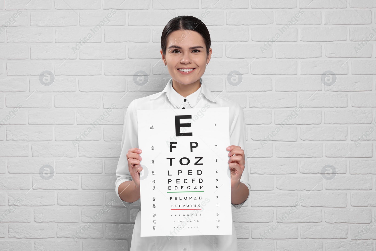 Photo of Ophthalmologist with vision test chart near white brick wall