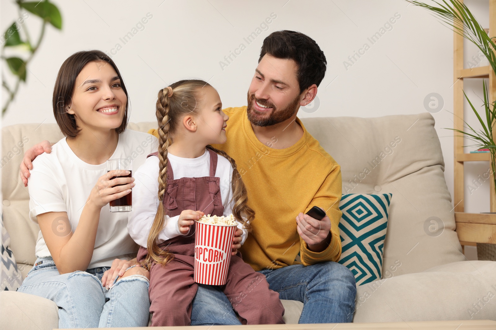 Photo of Happy family watching TV with popcorn on sofa indoors, space for text