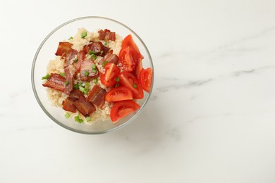 Photo of Tasty quinoa porridge with fried bacon and tomato in bowl on white marble table, top view. Space for text