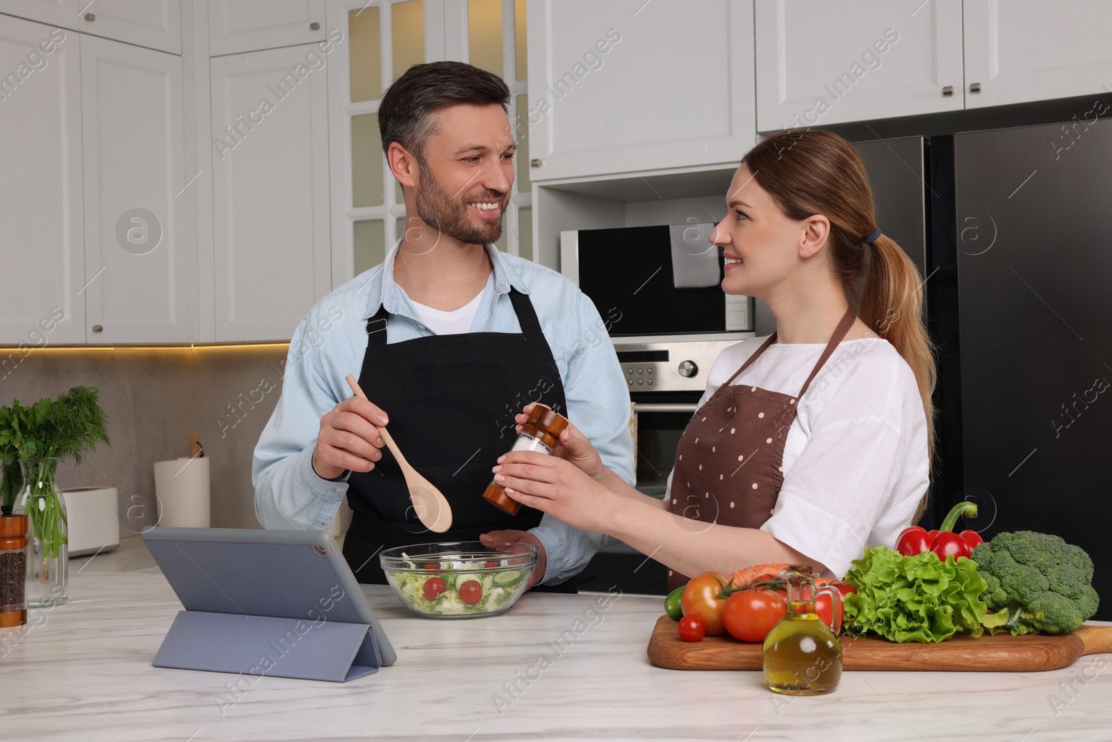 Photo of Happy couple reading recipe on tablet while cooking in kitchen. Online culinary book