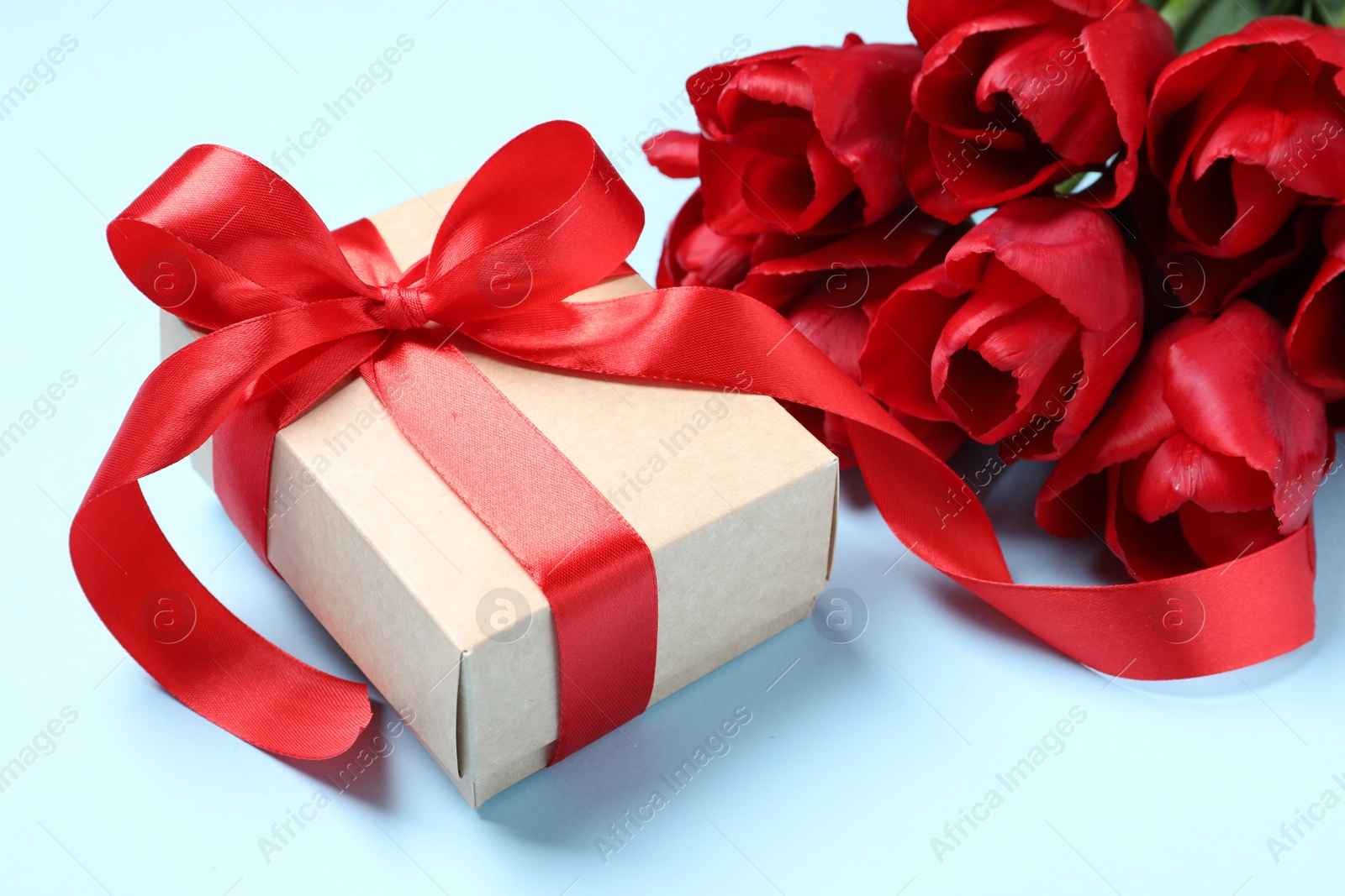 Photo of Beautiful gift box and bouquet of tulip flowers on light blue background, closeup