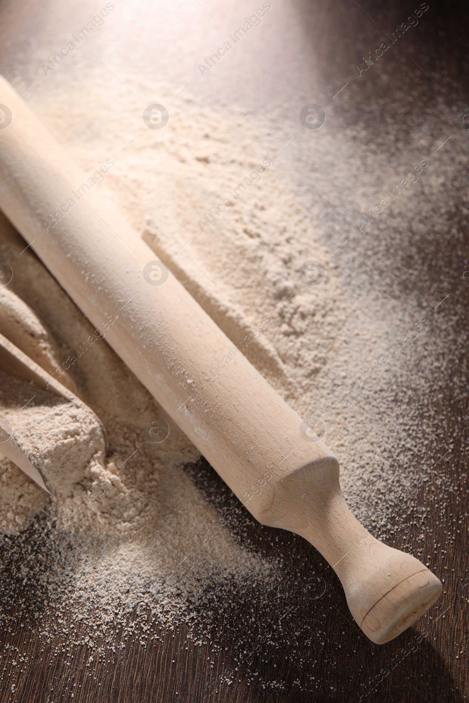 Photo of Pile of flour, rolling pin and scoop on wooden table, closeup