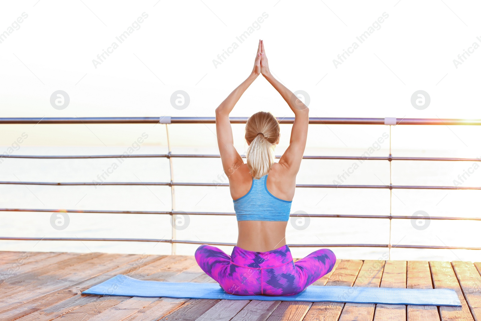 Photo of Young woman doing yoga exercises on pier in morning