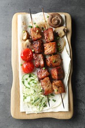 Photo of Delicious shish kebabs with vegetables and lavash on grey table, top view