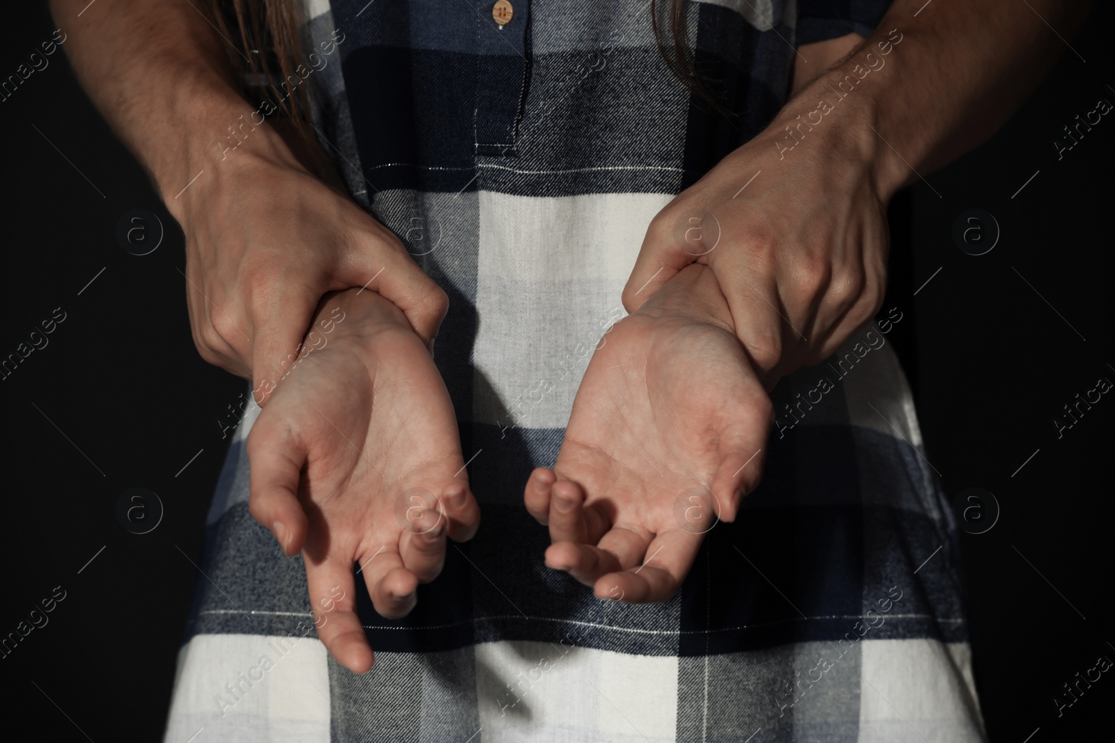 Photo of Man holding woman's hands on dark background, closeup. Stop sexual assault