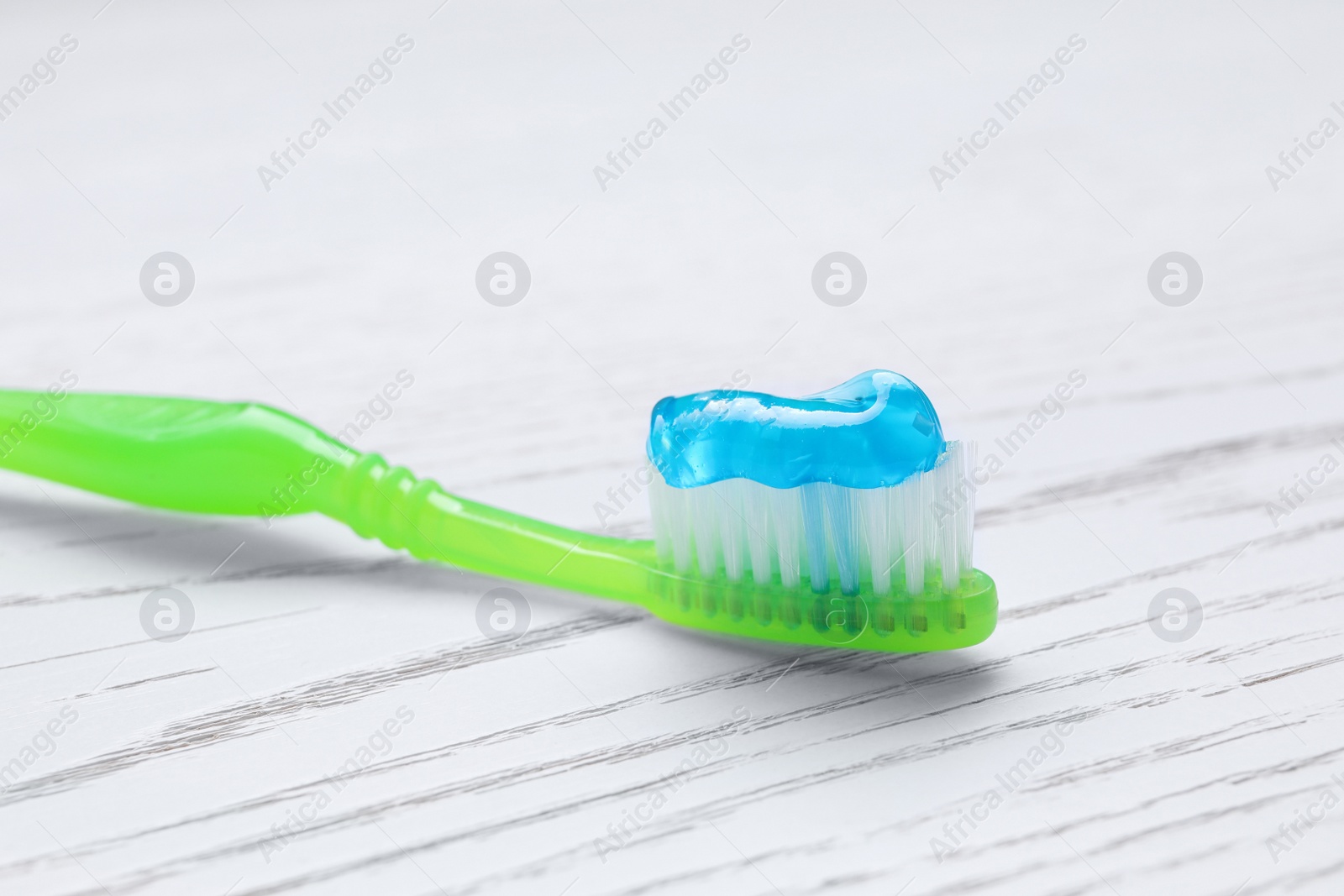 Photo of Brush with toothpaste on white wooden table, closeup