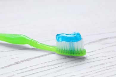 Photo of Brush with toothpaste on white wooden table, closeup
