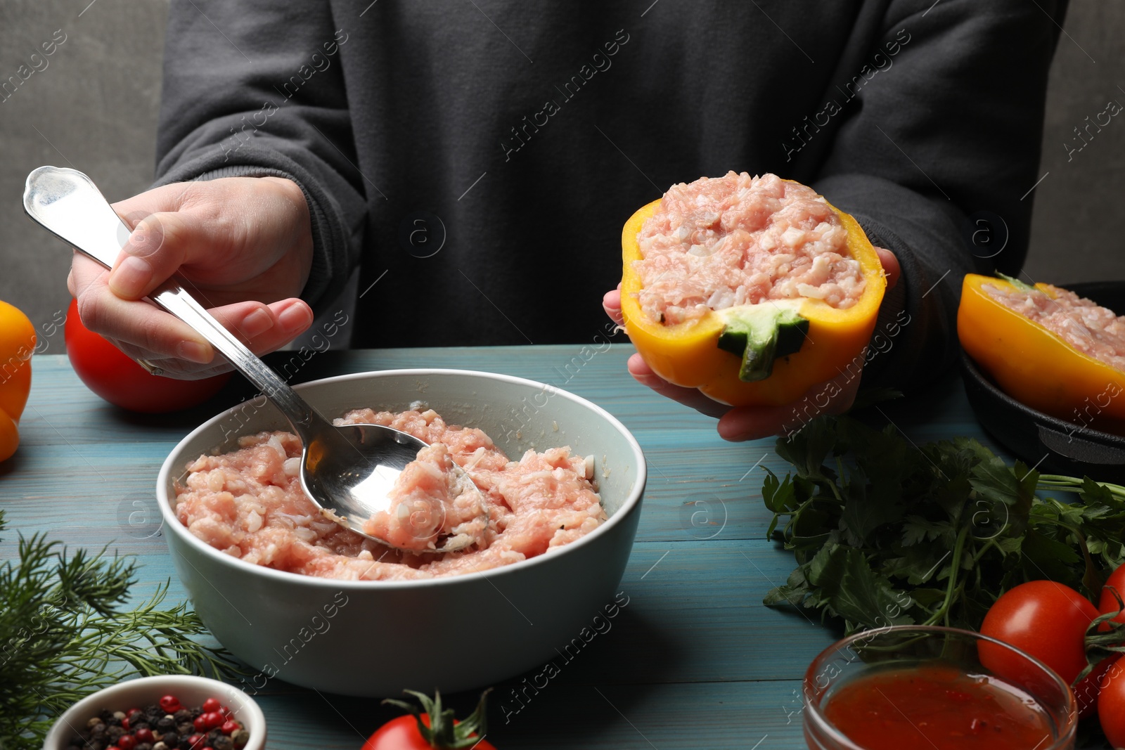 Photo of Woman making stuffed peppers with ground meat at light blue wooden table, closeup