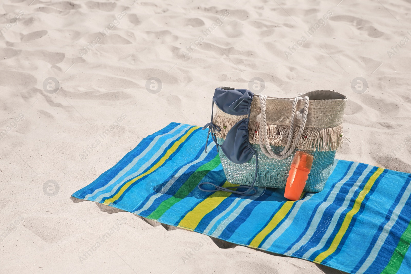 Photo of Striped beach towel and bag with accessories on sand