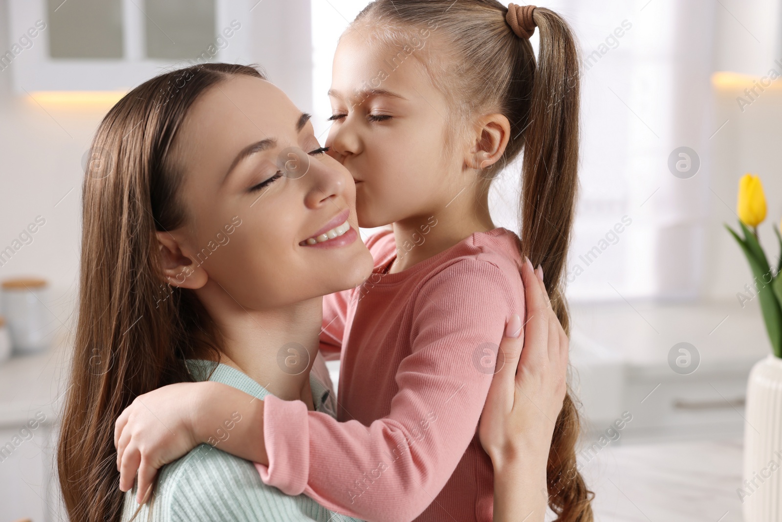 Photo of Cute daughter kissing her mom in kitchen