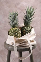 Photo of Bag with delicious ripe pineapples on stand against pink wall