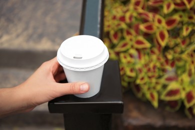 Woman with cardboard cup of coffee near flower bed outdoors, closeup