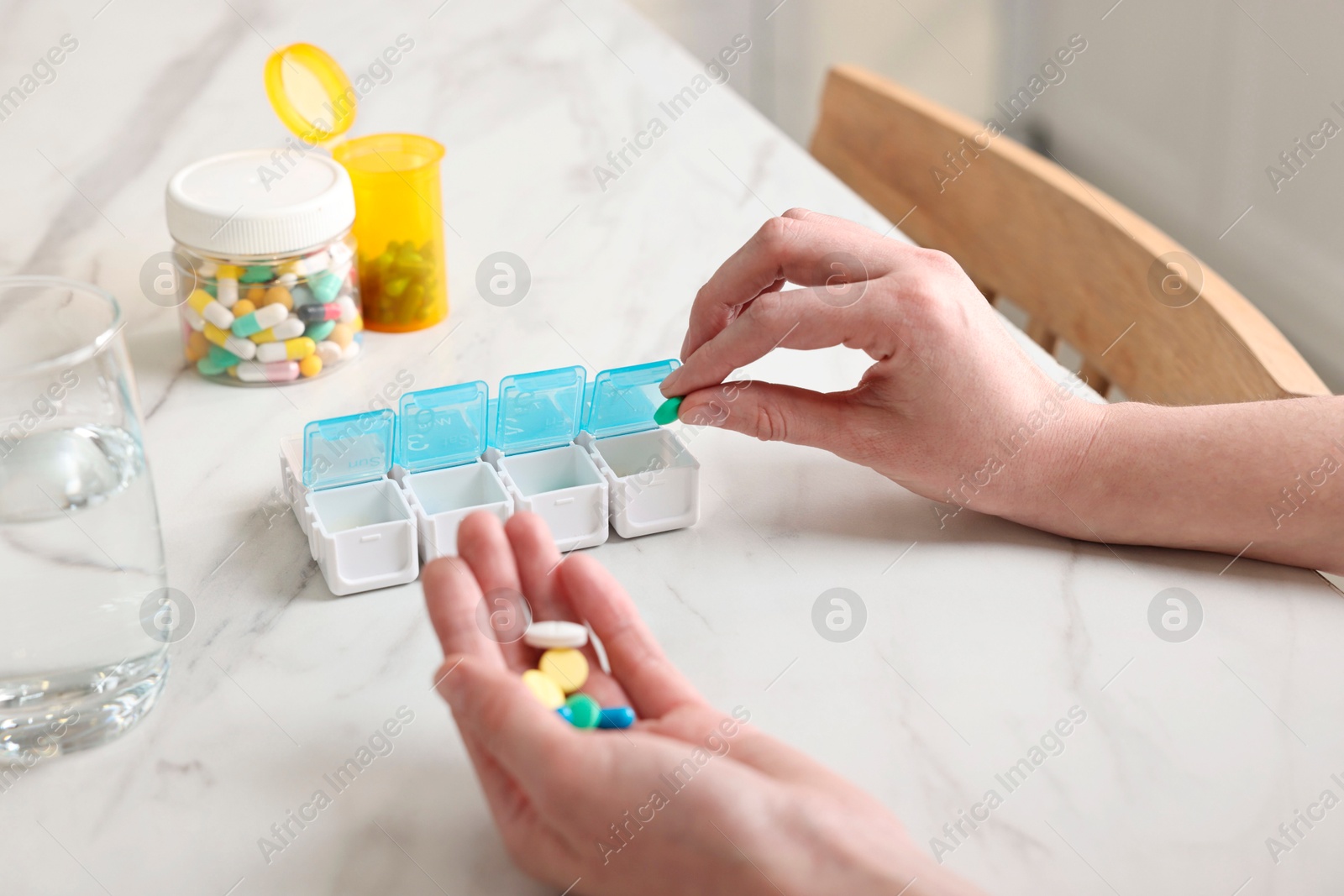 Photo of Woman with pills, organizer and glass of water at white marble table, closeup