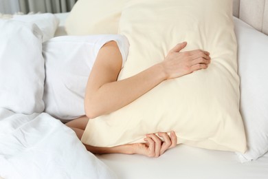 Photo of Sleepless woman covering head with pillow in bed at home