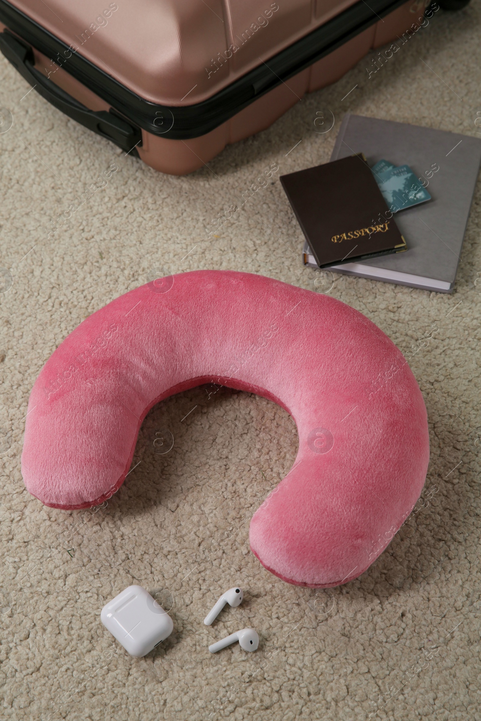 Photo of Pink travel pillow, suitcase, passport with credit cards and earphones on beige rug