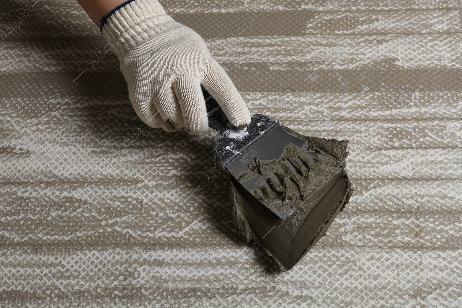 Photo of Worker spreading concrete on ceramic tile with spatula, closeup